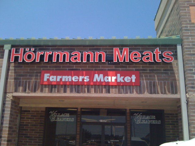 Signage of Hörmann Meats at a Farmers Market, featuring a brick facade and clear visibility of the business name, located in a shopping area.