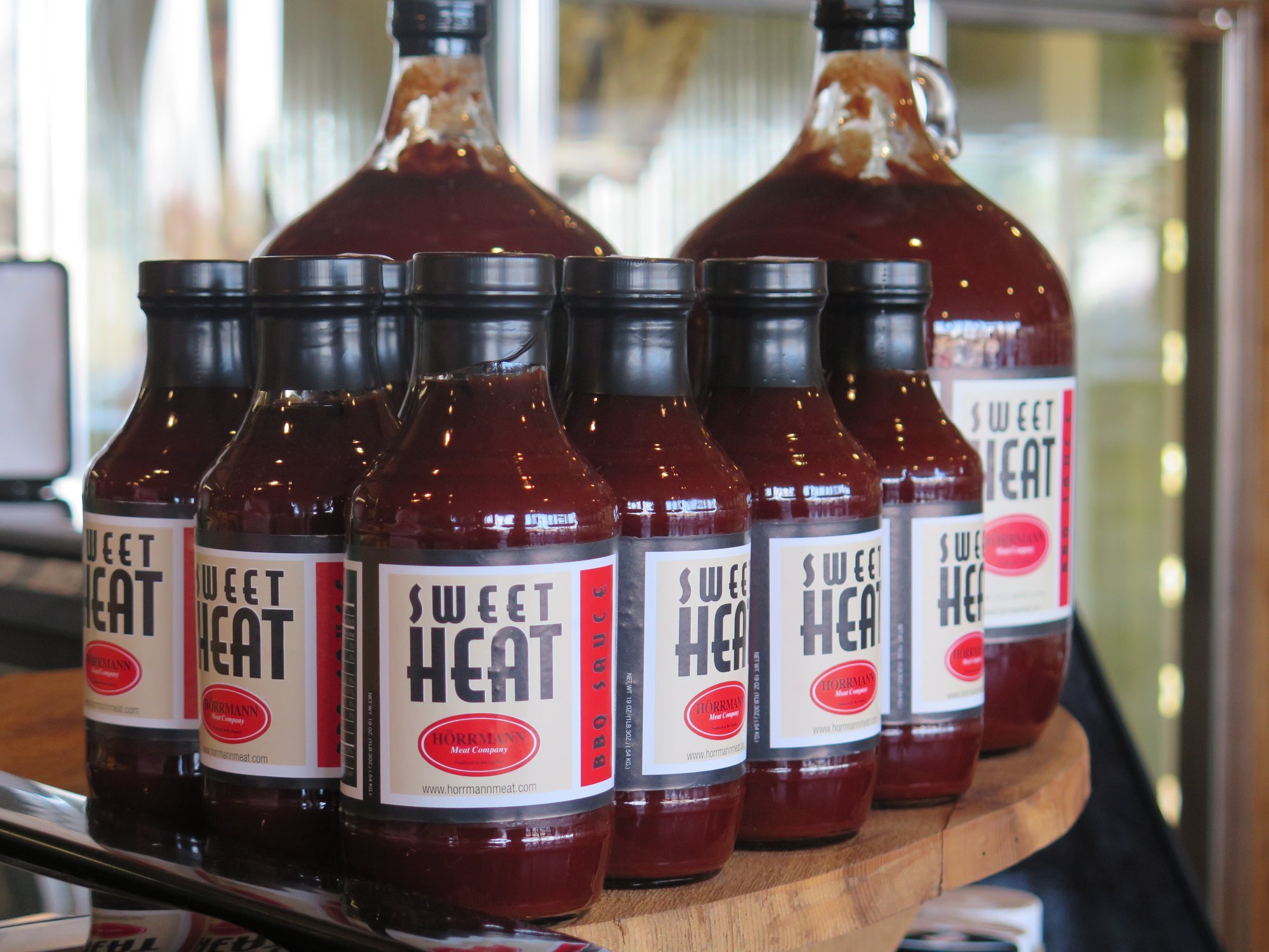 Horrmann+Meats,+Missouri+-+bbq Bottles of Sweet Heat barbecue sauce displayed on a wooden shelf, featuring a blend of sweet and spicy flavors, produced by Horrmann Meat Company.