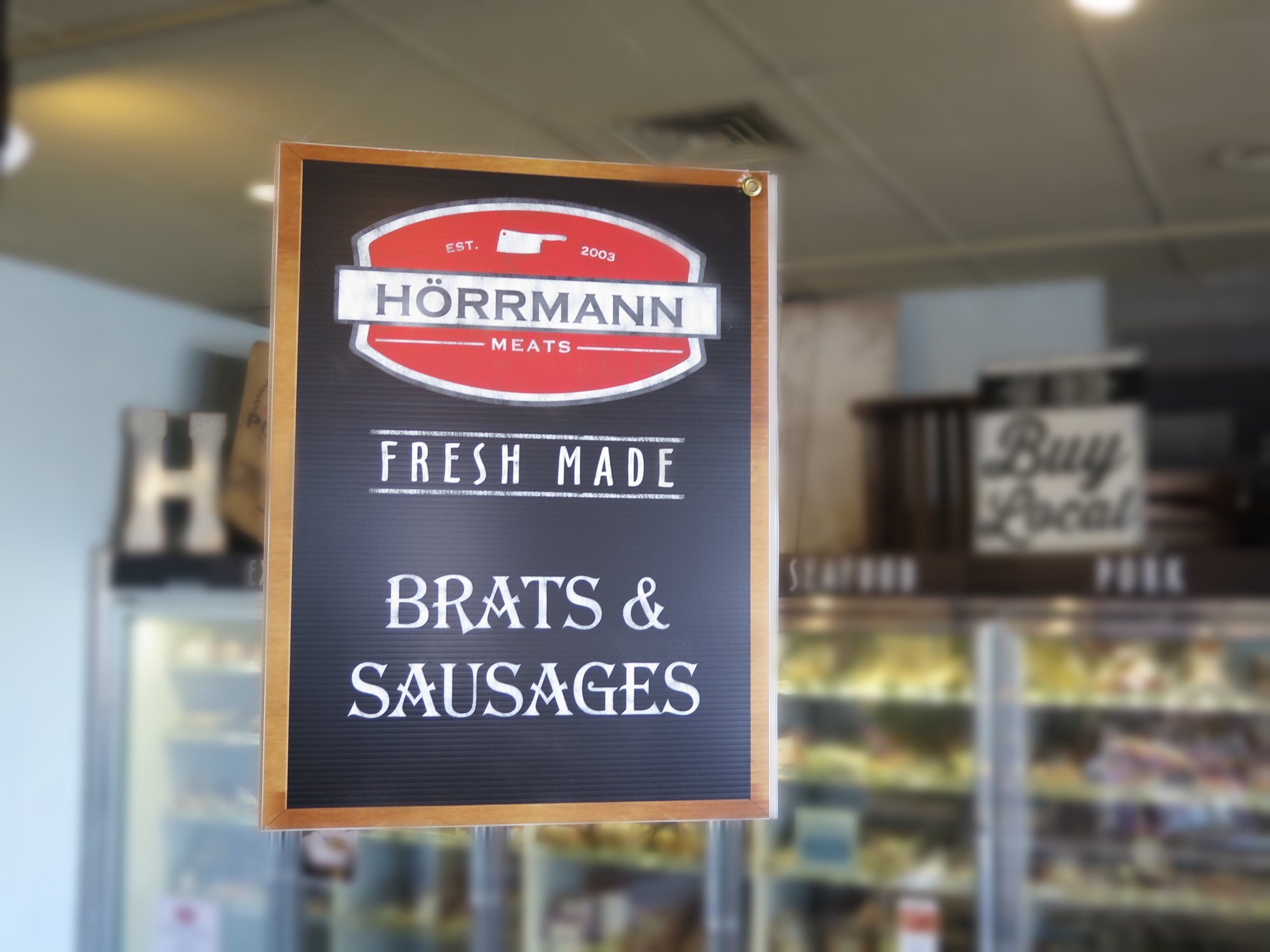 Sign for Hörmann Meats featuring fresh-made brats and sausages, displayed in a butcher shop.