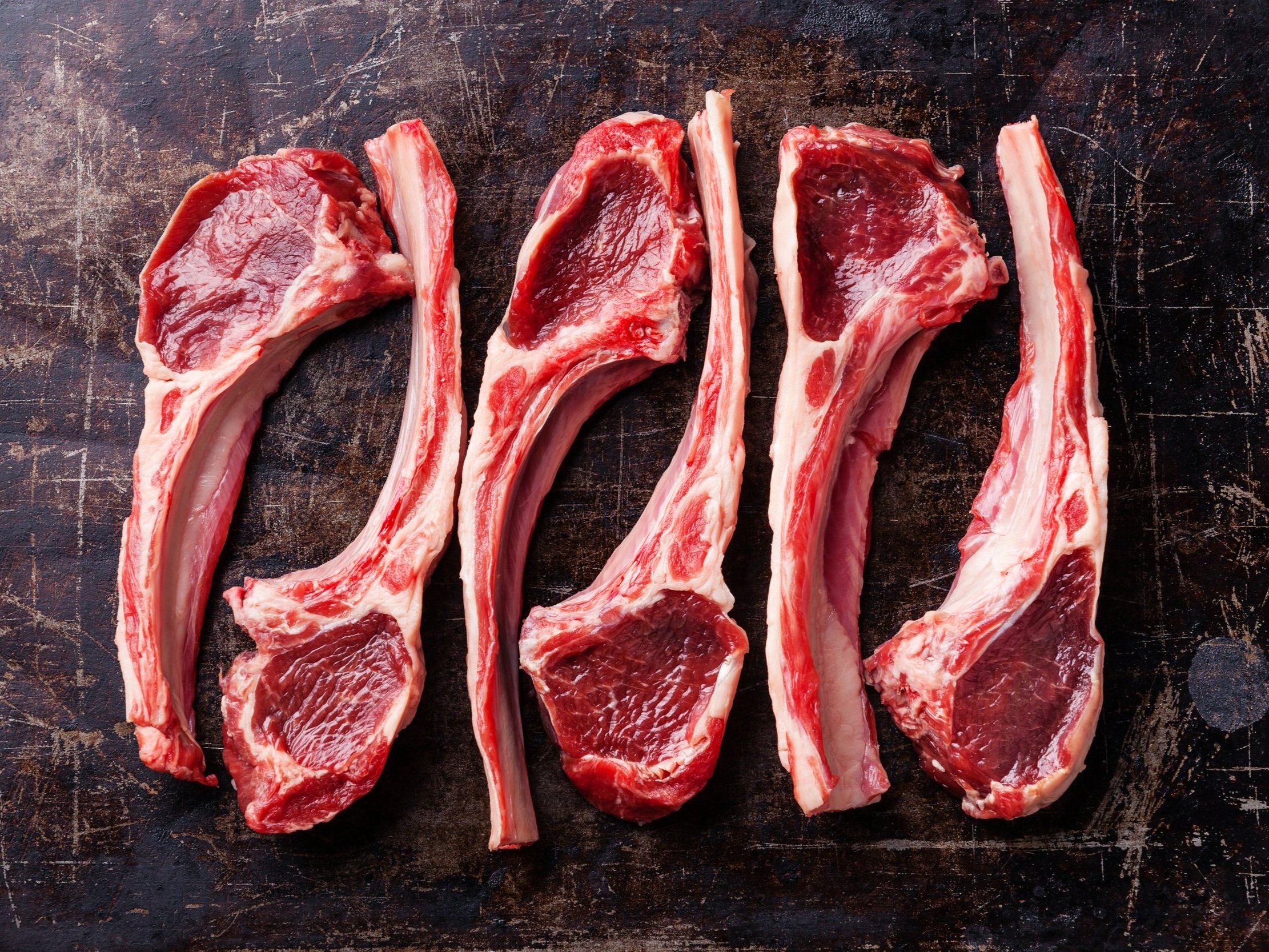 lamb_chops_raw Raw lamb chops arranged neatly on a rustic wooden cutting board, showcasing their rich red color and marbled texture, ideal for grilling or roasting.